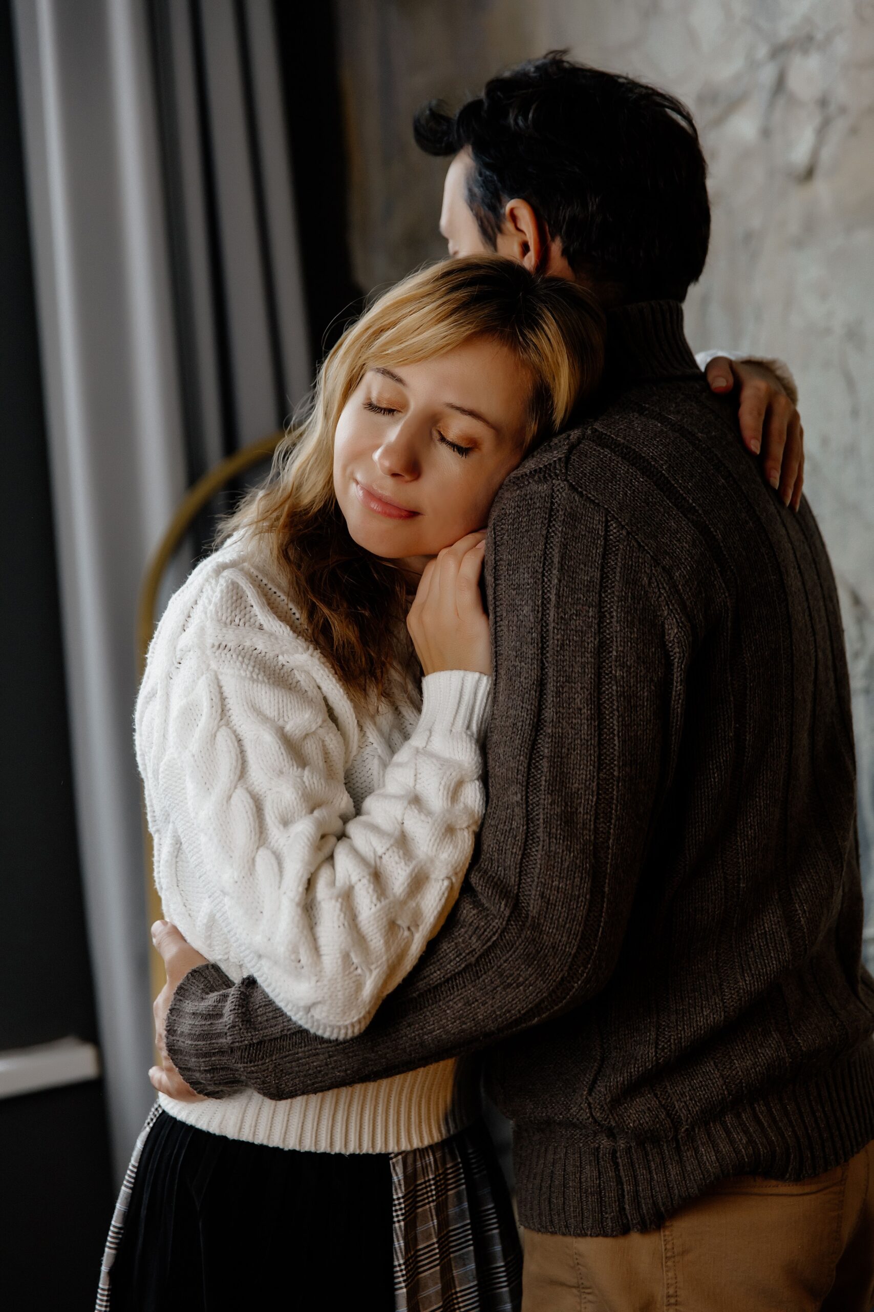 A loving couple shares an intimate embrace indoors, highlighting warmth and connection.